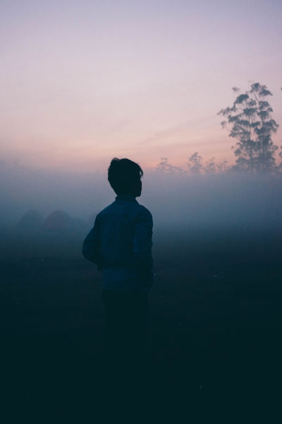 person in fog at twilight looking away into distance